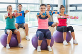 Fitness class sitting with dumbbells on exercise balls