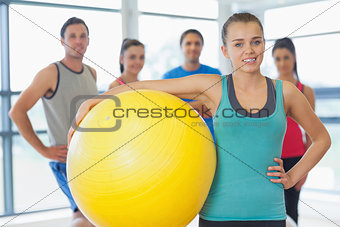 Instructor holding exercise ball with fitness class in background