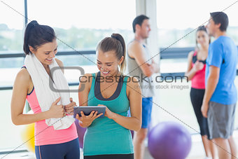 Fit women looking at digital table with friends chatting in background