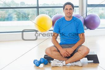 Young man sitting with dumbbells in fitness studio