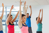 Side view of sporty people raising hands at yoga class