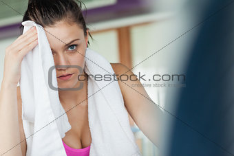 Tired woman wiping face while working on row machine