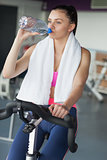 Tired woman drinking water while working out at spinning class