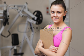 Smiling female trainer with clipboard in the gym
