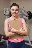 Smiling female trainer with clipboard in gym