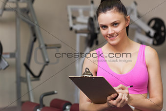 Smiling female trainer writing on clipboard in gym