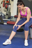 Healthy woman with an injured knee sitting in gym