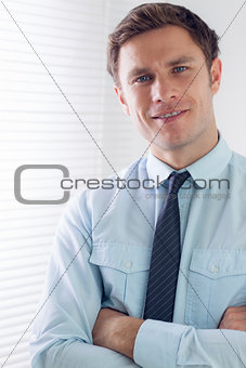 Elegant young businessman with arms crossed in office