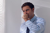 Businessman peeking through blinds while coughing