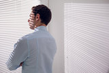 Businessman peeking through blinds in office