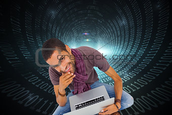 Composite image of man sitting on floor using laptop and smiling at camera