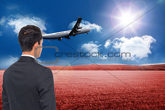 Composite image of businessman watching plane taking off