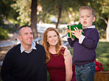 Young Boy Holding Christmas Gift in Park While Parents Look