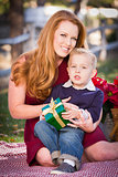 Young Boy Holding Christmas Gift with His Mom in Park