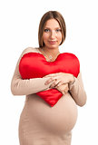 Smiling pregnant woman with heart shaped pillow over white