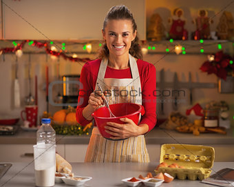 Happy young housewife whisking dough in christmas decorated kitc