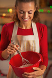 Happy young housewife using dough whisk