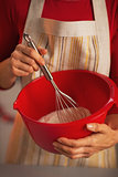Closeup on young housewife using dough whisk