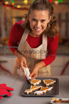 Smiling young housewife decorating christmas cookies in kitchen