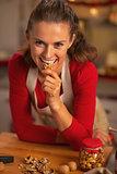 Happy young woman eating walnuts in kitchen