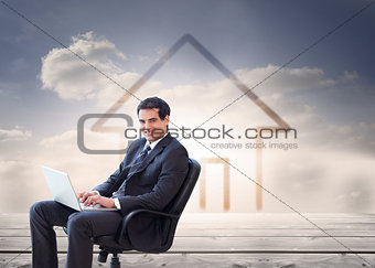 Composite image of young businessman sitting on an armchair working with a laptop