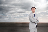 Composite image of serious businessman standing with his arms folded