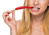 Closeup on teenage girl holding biting red chili pepper