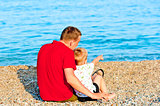 son and father sitting by sea