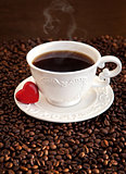 White cup of coffee with red heart on coffee beans 