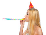 Profile portrait of teenage girl in cap blowing in party horn bl