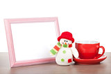 Blank photo frame, christmas snowman and coffee cup on wooden ta