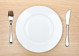 Empty white plate with silverware on wooden table