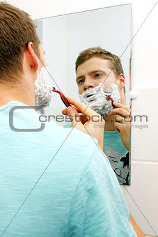 young man shaving his face, reflection in mirror