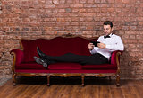 Businessman lying on a settee and reading tablet