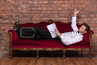 Businessman lying on a settee and reading paperwork