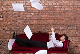 Businessman lying on a settee with flying papers