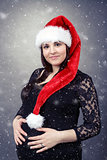 beautiful pregnant woman wearing santa hat and tenderly holding her tummy