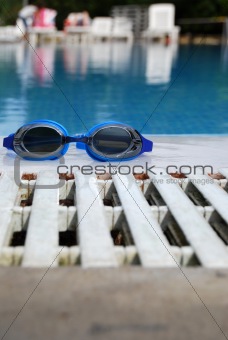 Swimming goggles by the side of an outdoor pool.