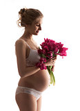 Beautiful young pregnant woman in lingerie holding flowers