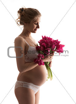Beautiful young pregnant woman in lingerie holding flowers