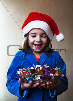 girl in wearinlg santa hat holds a dish with chocolates