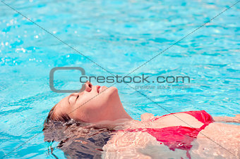 girl lying on the water with eyes closed in the pool
