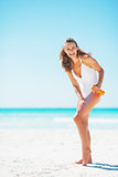 Full length portrait of smiling young woman applying sun screen 