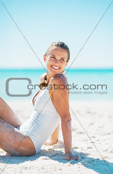 Happy young woman sitting on beach and looking on copy space