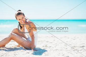 Smiling young woman sitting on beach and looking on copy space