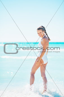 Full length portrait of happy young woman walking in sea