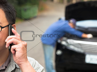 man Talking on Phone While Mechanic Fixes Car