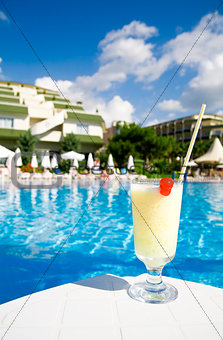 cocktail in glass on a background tourist resort and blue water of pool
