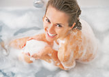 Smiling young woman playing with foam in bathtub