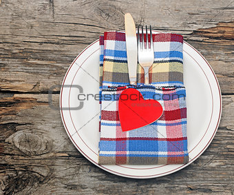 Cutlery in the colorful napkin and red heart on an empty plate